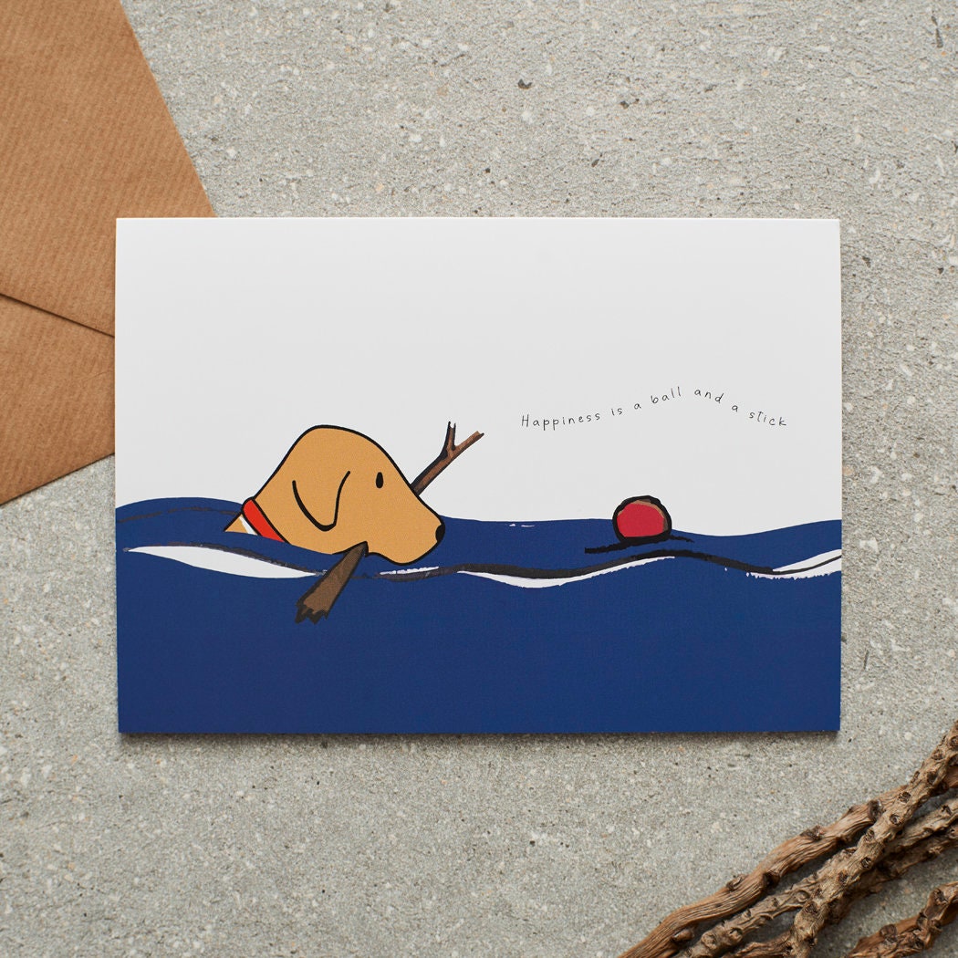 Swimming Fox Red Labrador card featuring a water-loving Fox Red Lab chasing a ball while holding a stick, with the words “Happiness is a ball and a stick” by Sweet William Designs