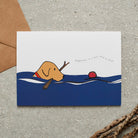 Swimming Fox Red Labrador card featuring a water-loving Fox Red Lab chasing a ball while holding a stick, with the words “Happiness is a ball and a stick” by Sweet William Designs