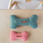 Green and orange tweed dog bone toys in two different sizes, displayed together on a wooden table