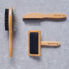 Sweet William bamboo dog grooming collection including — metal comb, slicker brush and double sided brush on grey stone surface, dog grooming gift set