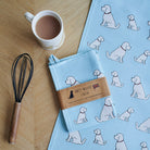Organic cotton Apricot Cockapoo / Labradoodle tea towel on a wooden table with a matching mug — organic cotton screen printed kitchen gifts for dog lovers by Sweet William Designs.