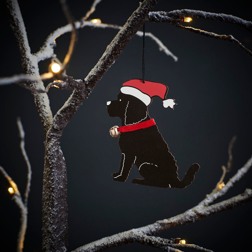 Black Cockapoo / Labradoodle Christmas tree decoration hanging on lit winter tree — wooden dog decoration with Father Christmas hat and jingle bell collar by Sweet William Designs
