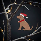 Chocolate Cocker Spaniel Christmas tree decoration hanging on lit winter tree — wooden dog decoration with Father Christmas hat and jingle bell collar by Sweet William Designs