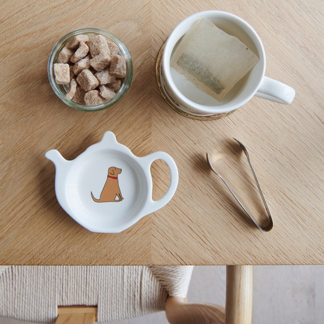 White teapot-shaped Fox Red Lab teabag dish with a fox-red dog illustration and red collar, beside a mug, sugar cubes and sugar tongs