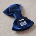 Close-up of the back of a navy velvet dog bow tie showing the elastic loops that attach to a collar and Sweet William branding