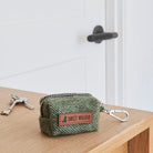 Green tweed dog poo bag holder with a zip, clip and Sweet William label, resting on a wooden table