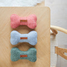 The full Sweet William tweed dog bone toy colour range in orange, grey and green, arranged together on a wooden table