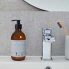 Dog Walkers Revival Hand Lotion in amber glass pump bottle on bathroom surface — vitamin E hand lotion, dog walker gift by Sweet William Designs