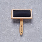 Bamboo slicker brush laid flat on grey stone surface with Sweet William branding — dog grooming gift