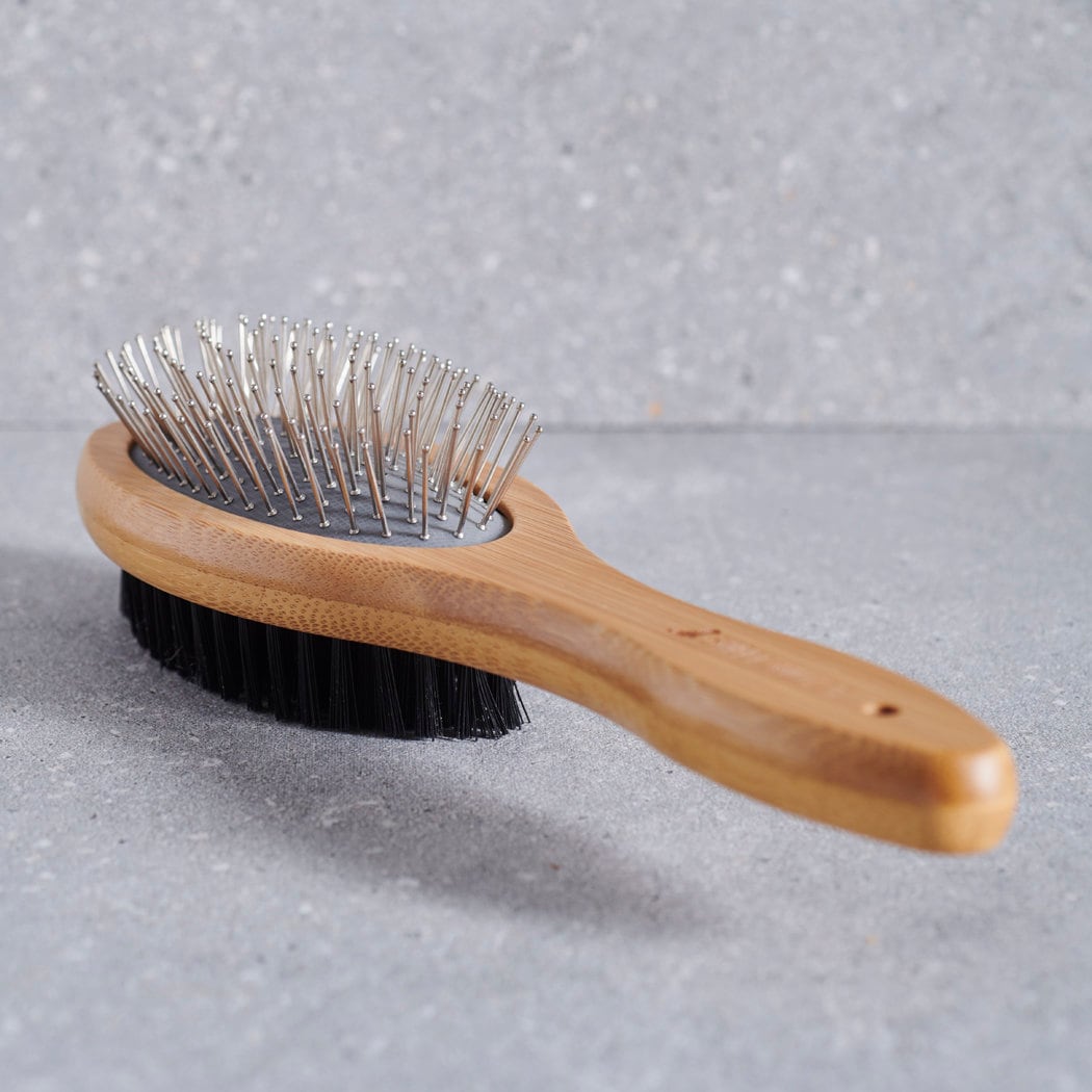 Bamboo double sided dog brush laid flat on grey stone surface — dog grooming brush by Sweet William Designs
