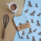 Organic cotton Chocolate Cocker Spaniel tea towel on a wooden table with a matching mug — organic cotton screen printed kitchen gifts for dog lovers by Sweet William Designs.