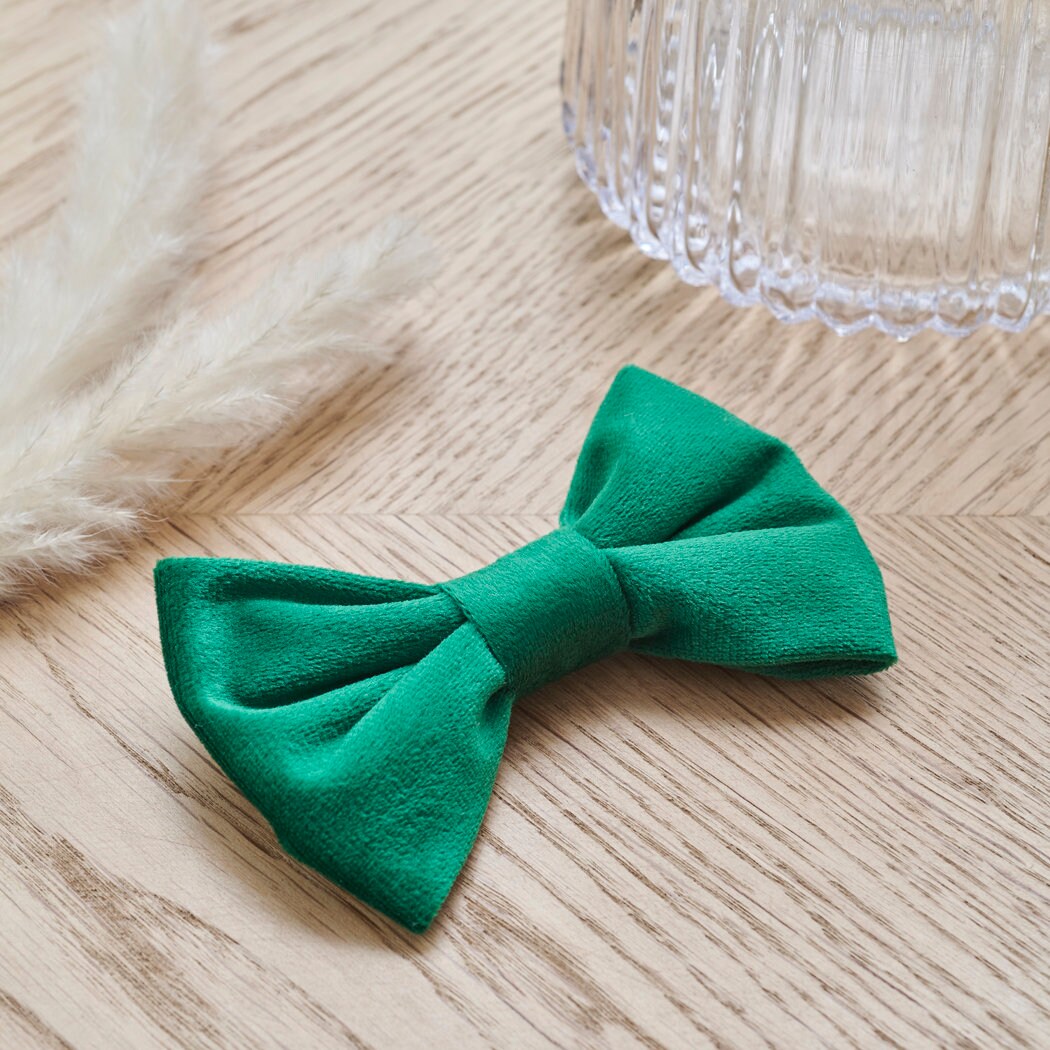 Soft green velvet dog bow tie resting on a wooden table, ready to add a smart finishing touch