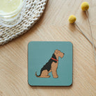 Airedale / Lakeland / Welsh Terrier coaster with a black and tan dog illustration on a blue background, on a wooden table
