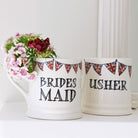 Bridesmaid and Usher mugs with Union Jack bunting, displayed together beside flowers as thoughtful wedding keepsakes