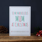 Funny Christmas card for Mum reading “To My Marvellous Mum at Christmas” and “With love from your favourite child”, with red and green lettering, a star border, pine cone and red berries.