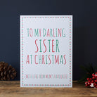 White Sister Christmas card with red and green lettering reading “To My Darling Sister at Christmas” and “With love from Mum’s favourite”, a star border, pine cone and red berries beside it.