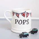 Ceramic Pops mug with hand-drawn Union Jack bunting and two small black toy cars, a thoughtful gift for a much-loved grandparent