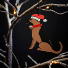 German Shepherd Christmas tree decoration hanging on lit winter tree — wooden dog decoration with Father Christmas hat and jingle bell collar by Sweet William Designs
